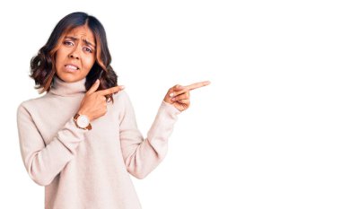 Balıkçı yaka kazak giyen genç, güzel, melez bir kadın endişeli ve gergin bir tarafı işaret ediyor. Endişeli ve şaşırmış bir ifadeyle. 