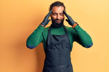 Genç Arap adam berber önlüğü takıyor. Baş ağrısı çekiyor. Acı ve migren yüzünden çaresiz ve stresli. Eller başının üstünde.. 
