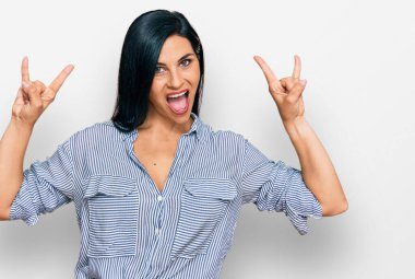 Kafkasyalı genç bir kadın gündelik kıyafetler giyip çılgın bir ifadeyle bağırıyor ve elleri havada rock sembolü yapıyor. Müzik yıldızı. ağır müzik konsepti. 