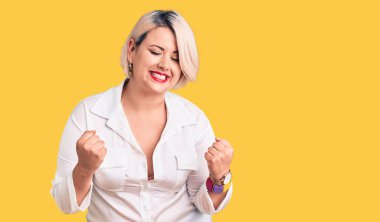 Genç sarışın ve cüsseli bir kadın rahat tişört giyiyor. Çok mutlu ve heyecanlı. Kolları havada, gülümseyen ve başarı için çığlık atan kazanan bir jest yapıyor. kutlama konsepti. 