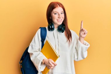 Sırt çantası takan ve elinde bir fikirle gülümseyen genç kızıl saçlı kız ya da soru işareti yapan mutlu yüzlü, bir numara. 