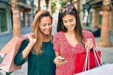 Güzel İspanyol anne ve kızı akıllı telefon kullanıyor ve şehirde alışveriş yapıyor..