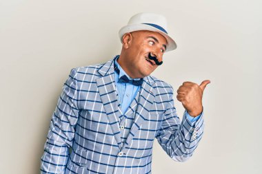 Klasik ve zarif moda tarzı olan bıyıklı olgun bir Orta Doğulu adam baş parmağını yana kaldırıyor ve ağzı açık gülümsüyor. 