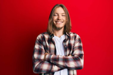 Uzun saçlı, sıradan kıyafetler giyen, kollarını kavuşturup kameraya gülümseyen yakışıklı beyaz adam. pozitif kişi. 