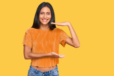 Genç, esmer, sıradan kıyafetler giyen, elleri büyük ve büyük bir işaret gösteren, ölçü sembolü olan Arap bir kadın. Kameraya bakıp gülümsüyor. ölçüm kavramı. 