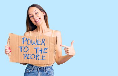 Güzel esmer, genç bir kadın gücü elinde tutuyor insanların bayrağına gülümsüyor mutlu bir şekilde el ve parmağıyla işaret ediyor. 