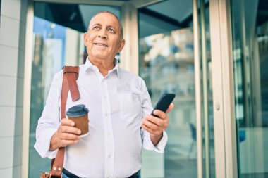 Beyaz saçlı kıdemli işadamı akıllı telefon kullanıyor ve şehirde kahve içiyor..