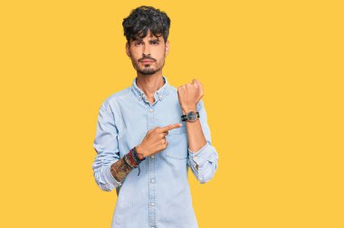 Gündelik kıyafetler giyen genç İspanyol adam saati, sabırsızlığı ve rahat bir ifadeyle kameraya bakmayı işaret ediyor. 