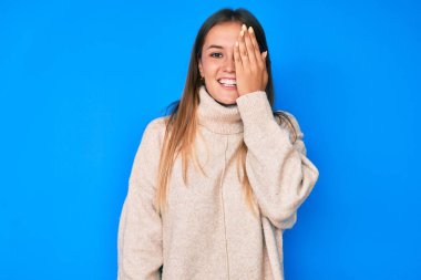 Güzel beyaz kadın yün kazak giyiyor bir gözünü eliyle kapatıyor, yüzünde kendine güvenen bir gülümseme ve şaşırtıcı bir duygu var.. 