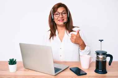 Orta yaşlı esmer, ofiste çalışan, operatör kulaklığı takan, mutlu ve olumlu gülümseyen, mükemmel ve onay tabelaları olan bir kadın. 