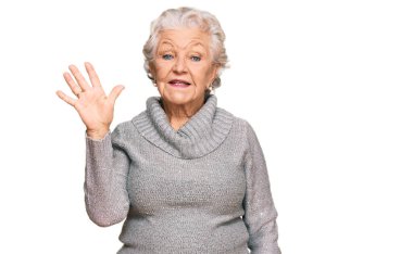 Kış süveteri giyen yaşlı, gri saçlı kadın gülümseyerek kendinden emin ve mutlu gülümserken parmaklarıyla beş numarayı gösteriyor.. 