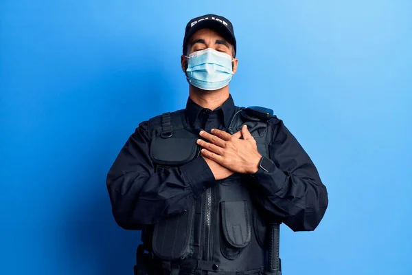 警察の制服を着た若いヒスパニック系の男と胸に手で笑みを浮かべて医療マスク 目を顔に感謝のジェスチャーで閉じます 健康の概念 — ストック写真