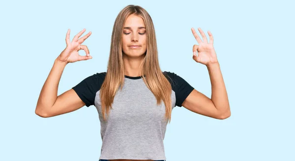 カジュアルな服を着た若いブロンドの女性がリラックスし 指で瞑想ジェスチャーを行う目を閉じて笑顔 ヨガのコンセプト — ストック写真