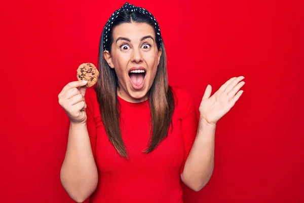 Young Beautiful Brunette Woman Holding Sweet Chocolate Cookie Isolated Red — ストック写真