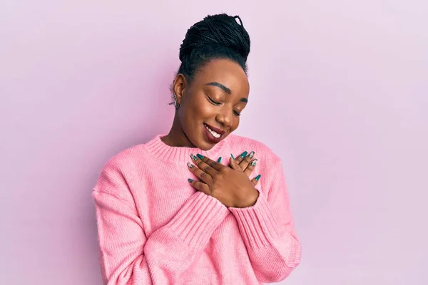 年轻的非洲裔美国女人穿着休闲的冬季毛衣 双手放在胸前笑着 闭着眼睛 脸上挂着感激的手势 健康概念 — 图库照片