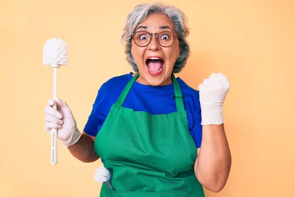 Mulher Hispânica Sênior Vestindo Avental Segurando Escova Gritando Orgulhoso Celebrando — Fotografia de Stock