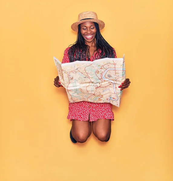 年轻美丽的非洲女人穿着夏装 戴着帽子 笑容满面 脸上挂着笑容跳过孤立的黄色背景的城市地图 — 图库照片