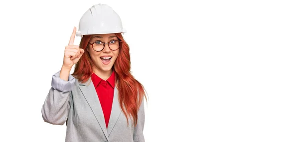 年轻的红头发女人戴着建筑师的硬礼帽 指指点点地提出了一个成功的想法 又兴奋又快乐第一大 — 图库照片