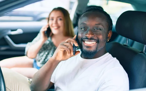 年轻的跨种族夫妇高兴地在车里用智能手机交谈 — 图库照片