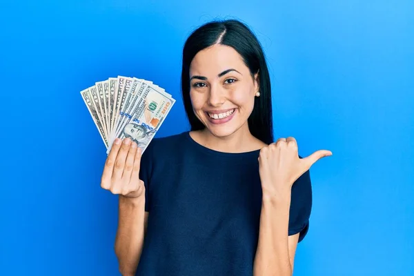 Beautiful Young Woman Holding Dollars Pointing Back Hand Thumbs Smiling — Stock Photo, Image