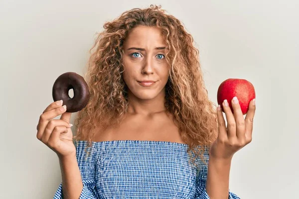 美しい白人のティーンエイジャーの女の子は赤いリンゴを保持し 問題のために動揺を眉をひそめて 懐疑的かつ神経をドーナツ 否定的な人 — ストック写真