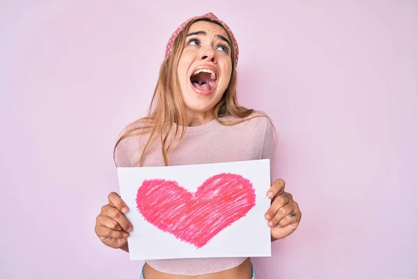 Joven Hermosa Mujer Rubia Sosteniendo Corazón Dibujar Enojado Loco Gritando — Foto de Stock