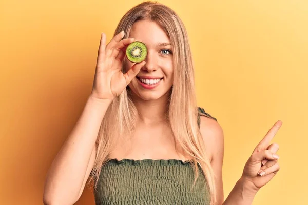 Young Blonde Woman Holding Kiwi Smiling Happy Pointing Hand Finger — ストック写真