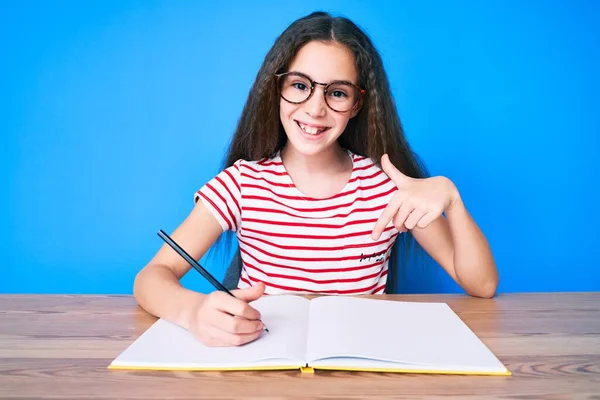 Menina Hispânica Bonito Sentado Mesa Escrevendo Livro Sorrindo Feliz Apontando — Fotografia de Stock