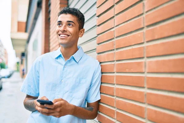 Νεαρός Λατίνος Άνθρωπος Χαμογελά Χαρούμενος Χρησιμοποιώντας Smartphone Ακουμπά Στον Τοίχο — Φωτογραφία Αρχείου