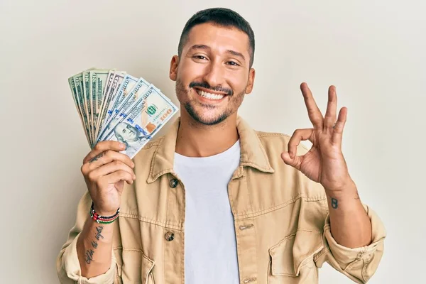 Dolarları tutan yakışıklı adam parmaklarıyla imza atıyor, gülümsüyor ve mükemmel bir sembol oluşturuyor. 