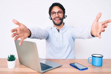 Ofiste çalışan yakışıklı İspanyol bir adam operatör kulaklığı takmış kameraya sarılıp gülümsüyor. Mutluluğu kucaklayan neşeli bir ifade.. 