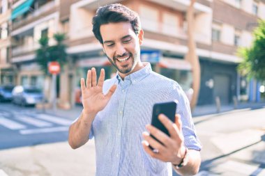 Genç İspanyol gülümseyen adam şehirde akıllı telefon kullanarak video araması yapıyor..