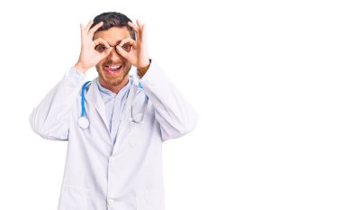 Doktor üniforması giyen yakışıklı genç bir adam. Dürbün gibi jest yapıyor. Dilini çıkarıyor, gözleri parmaklarından bakıyor. çılgın ifade. 