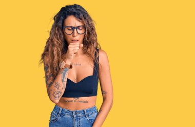 Günlük giysiler ve gözlük takan Latin kökenli genç bir kadın kendini iyi hissetmiyor ve soğuk algınlığı veya bronşitin belirtisi olarak öksürüyor. sağlık hizmeti kavramı. 