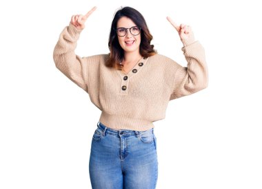 Güzel, genç, esmer bir kadın, günlük kıyafetler ve gözlük takıyor, şaşkın şaşkın gülüyor, parmaklarıyla işaret ediyor ve kollarını kaldırıyordu.. 