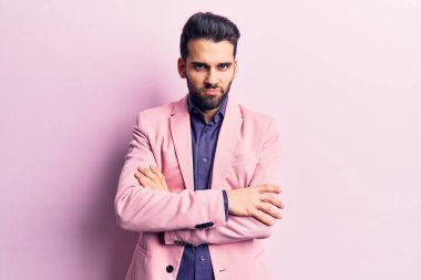 Sakallı, zarif ceketli, kuşkucu ve gergin, yüzünde çapraz kollu tasvip etmeyen genç yakışıklı bir adam. negatif kişi. 