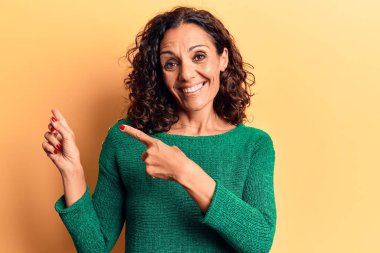 Orta yaşlı güzel bir kadın sıradan bir süveter giyiyor gülümsüyor ve kameraya bakıyor iki eliyle ve parmaklarıyla yandan işaret ediyor.. 