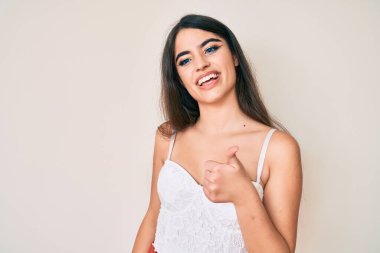 Esmer genç kız zarif poz veriyor ve elleriyle mutlu bir jest yapıyor. Kameraya bakıp başarıyı gösteren ifade. 