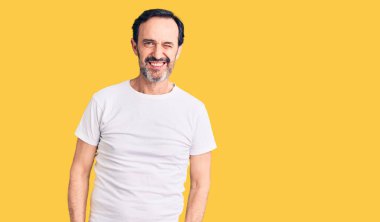 Orta yaşlı yakışıklı bir adam, sıradan bir tişört giyiyor, kameraya seksi bir ifadeyle bakıyor, neşeli ve mutlu bir yüz ifadesi var.. 