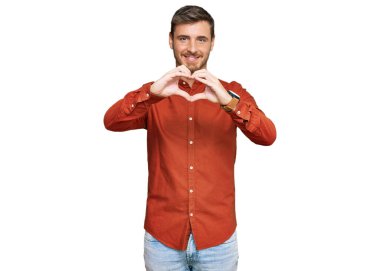 Yakışıklı, beyaz, günlük kıyafetler giyen, aşık gülümseyen, elleriyle kalp sembolü yapan bir adam. romantik kavram. 