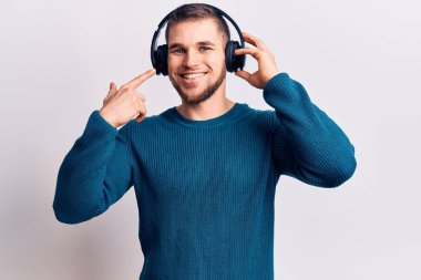 Genç yakışıklı adam kulaklık takarak müzik dinliyor mutlu bir şekilde el ve parmak işareti yapıyor. 