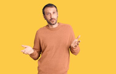 Sıradan kıyafetler giyen, elleri ve kolları havada, kafası karışmış genç ve yakışıklı bir adam. şüphe kavramı. 