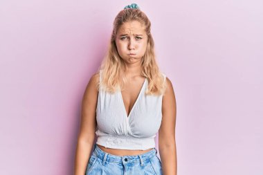 Sıradan kıyafetler giyen genç sarışın kız komik yüzlü yanakları şişiriyor. Havayla şişmiş ağız, çılgın bir ifade.. 