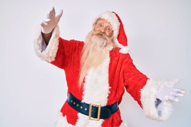 Gri saçlı, uzun sakallı, Noel Baba kostümlü, pantolon askısı takmış kameraya bakıp sarılmak için gülümseyen yaşlı bir adam. Mutluluğu kucaklayan neşeli bir ifade.. 