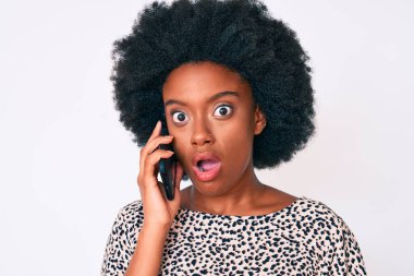 Genç Afro-Amerikalı kadın akıllı telefondan konuşuyor. Korkmuş ve ağzı açık bir şekilde şaşırmış, inançsız bir yüz ifadesi. 