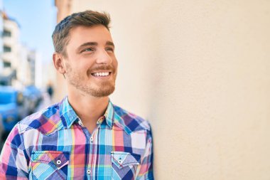 Beyaz bir adam gülümsüyor. Şehrin duvarına yaslanıyor..