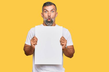 Orta yaşlı, boş afiş tutan yakışıklı bir adam ağzı açık kalmış, korkmuş ve şaşırmış bir şekilde şaşkınlık içinde, inançsız bir yüz. 