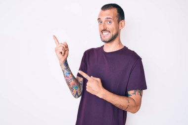 Dövmeli genç, sıradan kıyafetler giyen, gülümseyen ve kameraya bakan iki eli ve parmakları yanda olan yakışıklı bir adam.. 