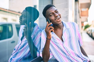 Genç Afrikalı Amerikalı gülümseyen adam şehrin caddesindeki akıllı telefonda mutlu bir şekilde konuşuyor..