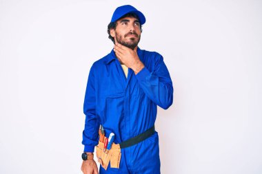 Kıvırcık saçlı yakışıklı genç adam ve ayı gibi giyinen tamirci üniforması ağrılı boynuna dokunuyor, boğaz ağrısı, grip salgını ve enfeksiyon. 